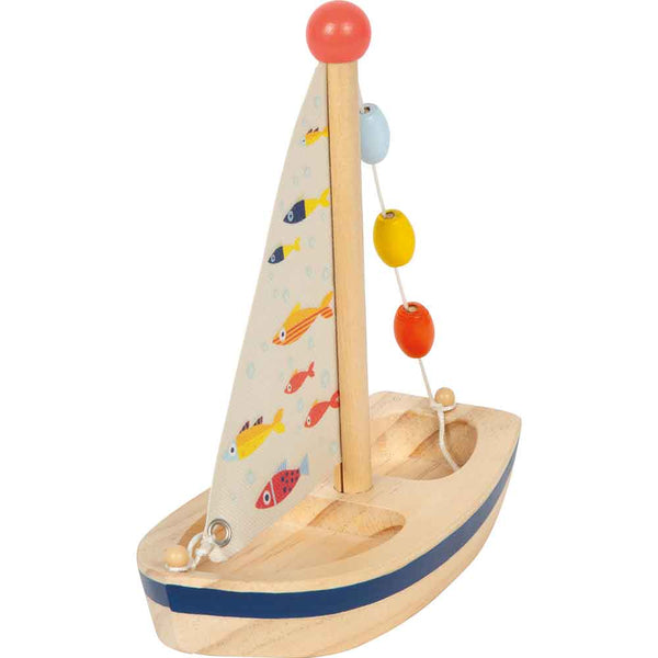 Ein kleines Holzspielzeug-Segelboot mit einem fischgemusterten Segel und vier bunten Perlen an einer Schnur entlang des Mastes.