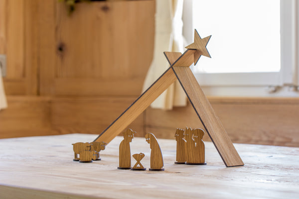 Minimalistische Holzkrippe mit Figuren und einem Stern auf einem Holztisch am Fenster.