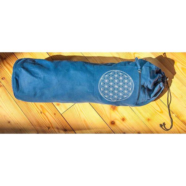 Eine blaue Yogamattentasche mit weißem geometrischem Muster, die auf einem Holzboden im Sonnenlicht liegt.