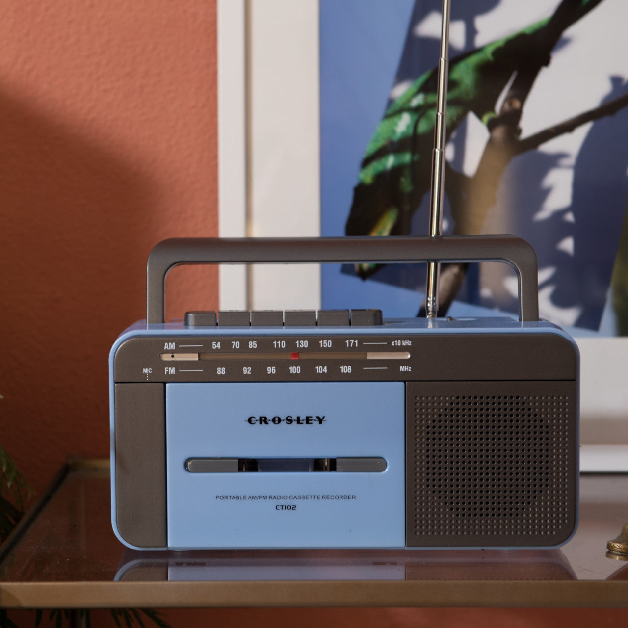 Ein Crosley Kassettenspieler – Blau/Grau liegt auf einer Glasoberfläche neben einem gerahmten Foto.