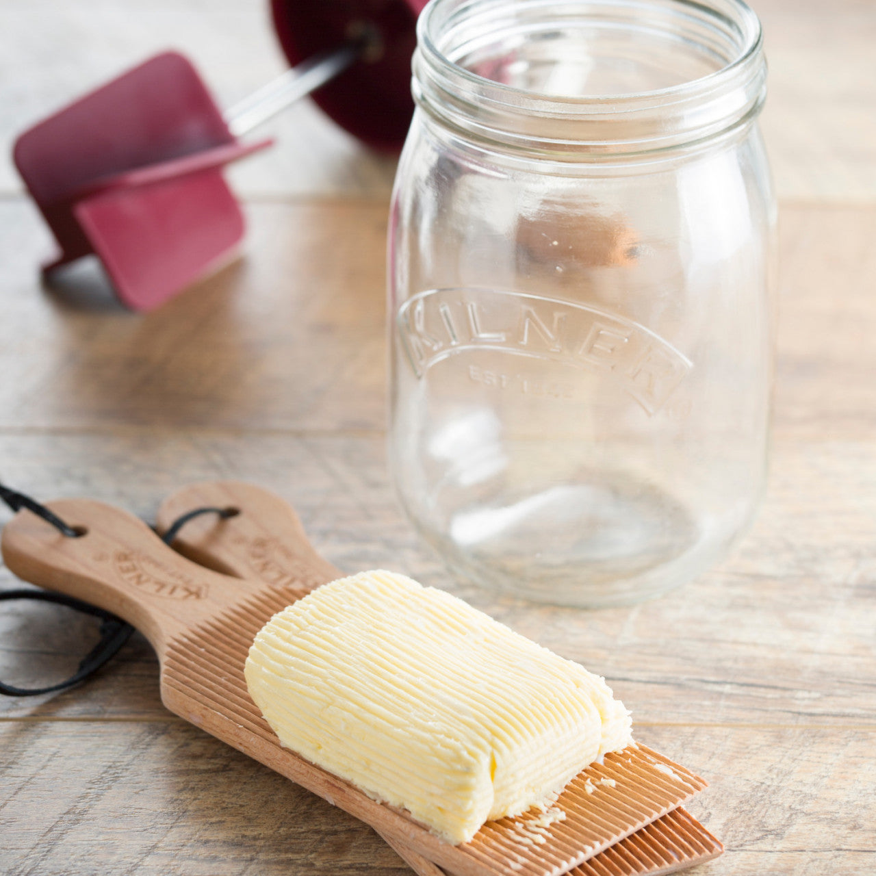 Ein 1-Liter-Glasgefäß von Butter Fass steht neben einem hölzernen Butterpaddel, das ein Stück Butter auf einer Holzoberfläche hält.