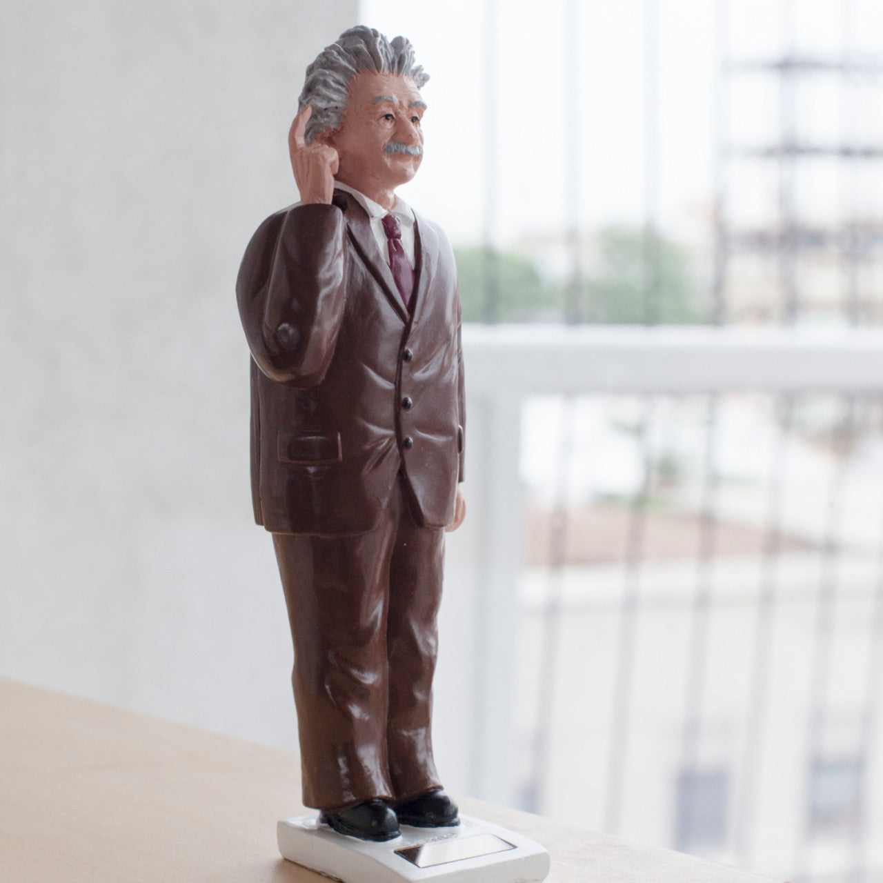 Eine kleine „Dekofigur Einstein mit Solarantrieb“ zeigt einen Mann im braunen Anzug mit weißen Haaren, der auf der Fensterbank steht und sein Ohr berührt.