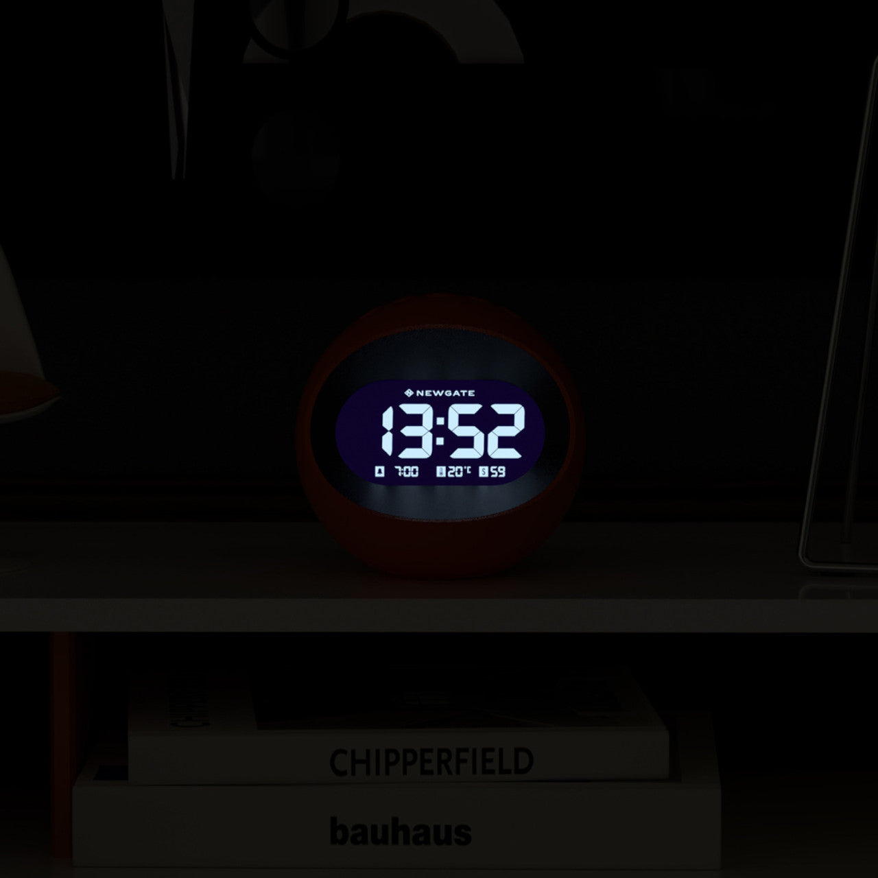 Eine digitale LCD-Wecker-Uhr von Zentrum der Erde – Orange zeigt 13:52 Uhr auf einem Regal neben Büchern an, darunter eines mit dem Titel CHIPPERFIELD.