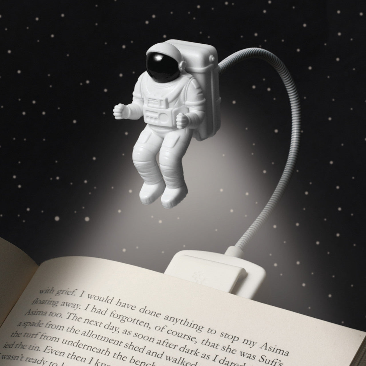 Die Leselampe Spaceman - 2 LEDs in Form eines Astronauten beleuchtet ein offenes Buch vor einem Sternenhimmel.