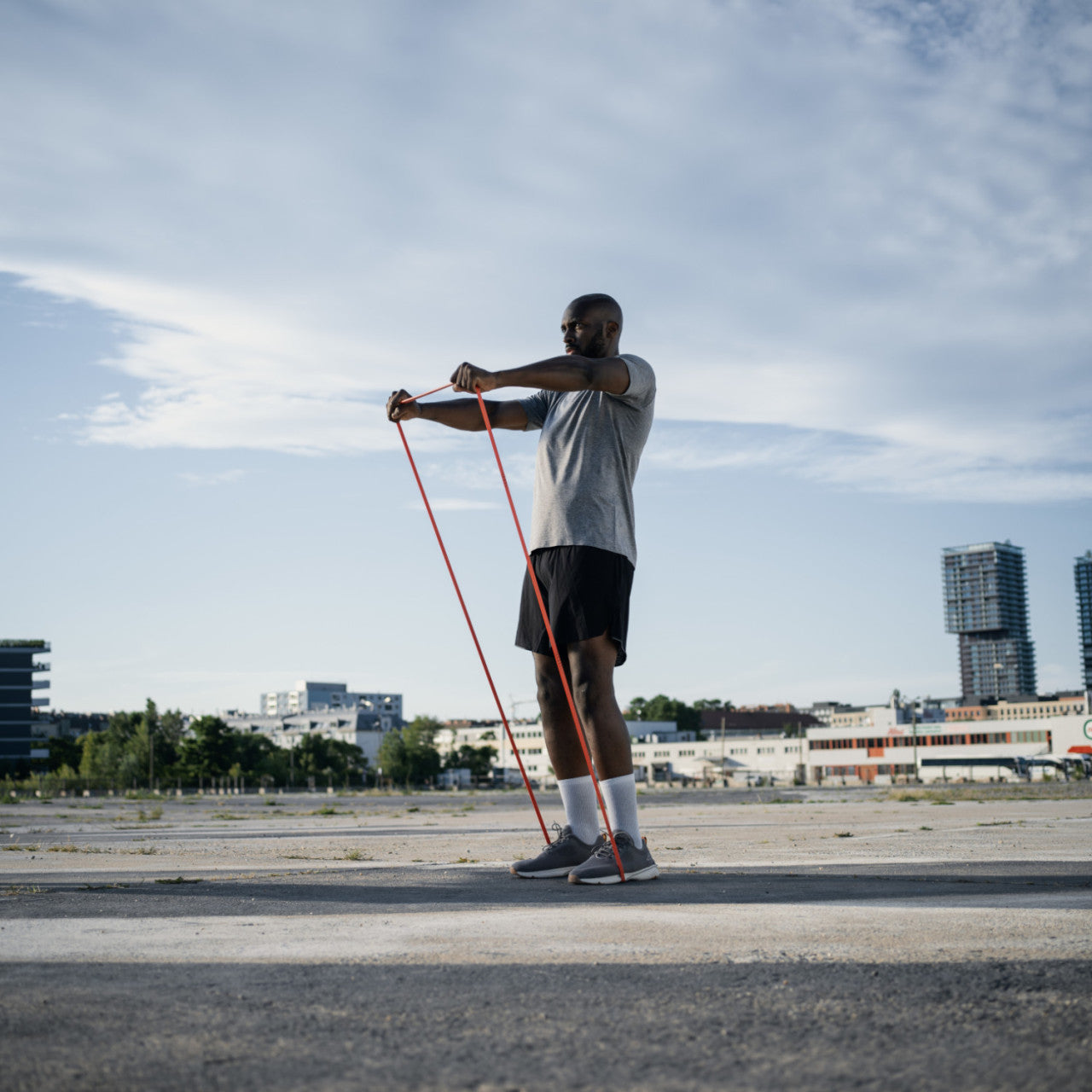 Mann trainiert im Freien mit dem STRAFFR Smart Fitnessband (stark), steht auf dem Bürgersteig mit Gebäuden im Hintergrund und verwendet die Begleit-App.