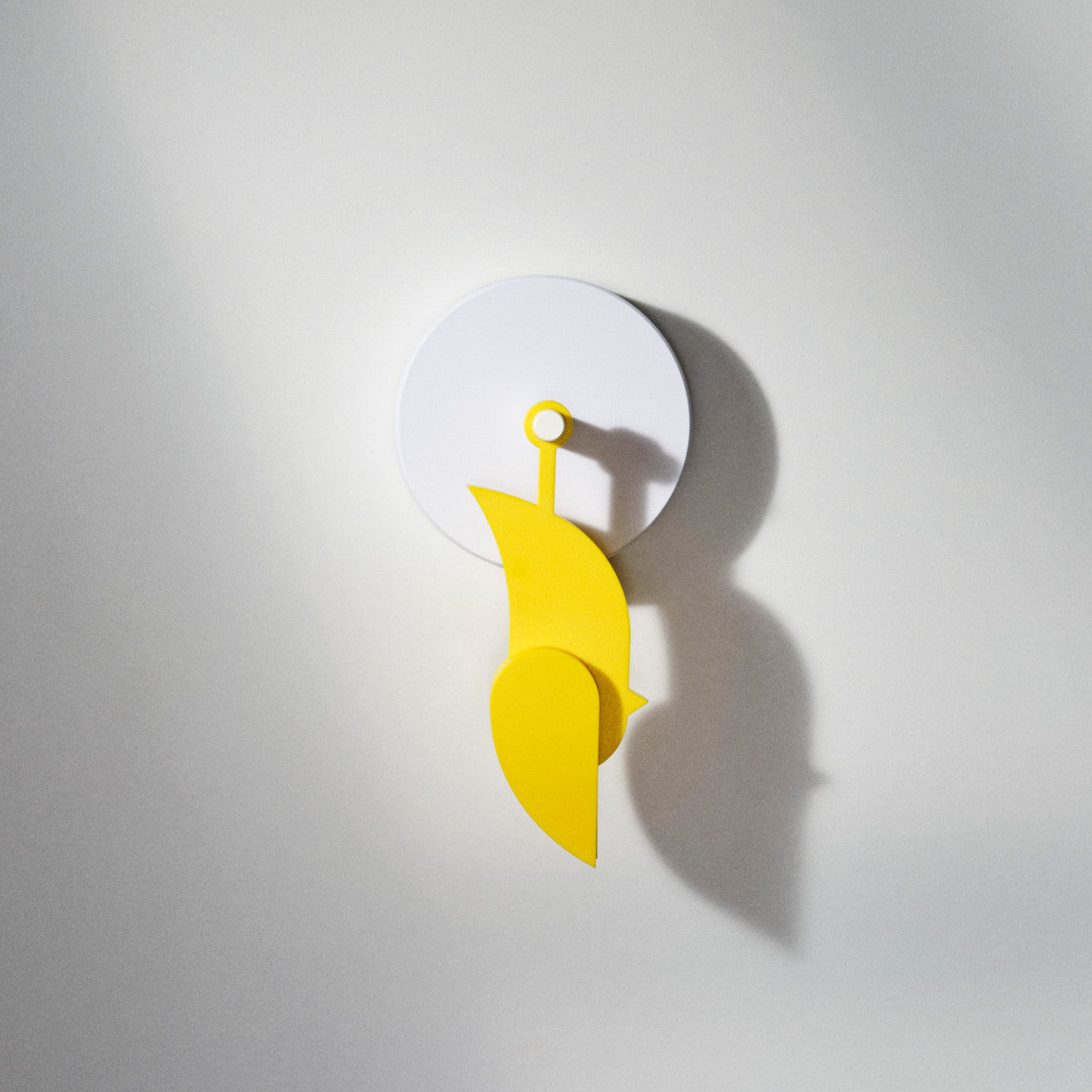 Frischluftmonitor Birdie 2.0 mit CO2-Sensor in Gelb, abstrakte Hängedekoration mit weißer runder Basis, wirft einen Schatten auf eine helle Wand.