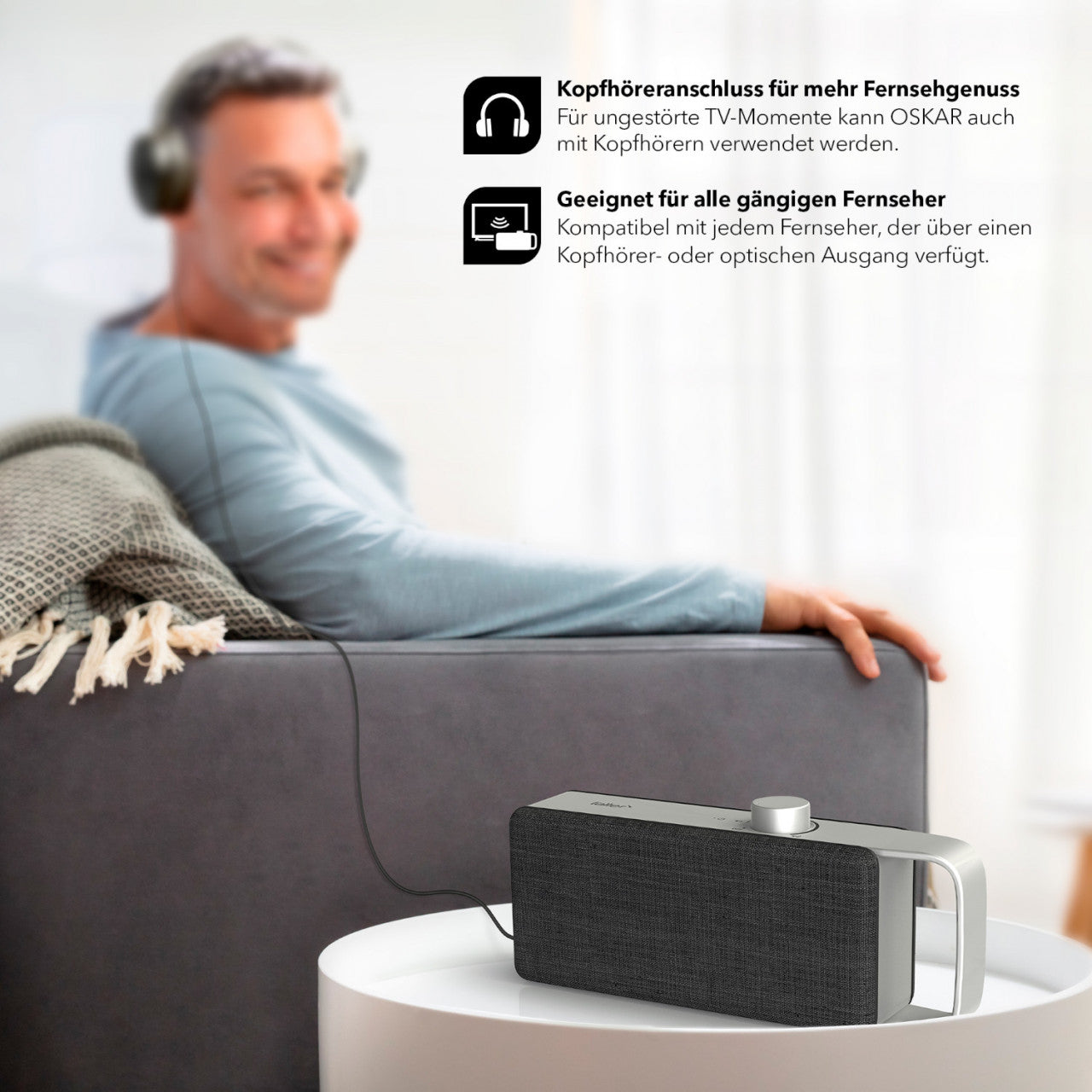 Ein Mann sitzt auf einem Sofa und trägt Kopfhörer, die an den tragbaren TV-Sprachverstärker OSKAR angeschlossen sind. Produktinformationen werden auf Deutsch angezeigt.