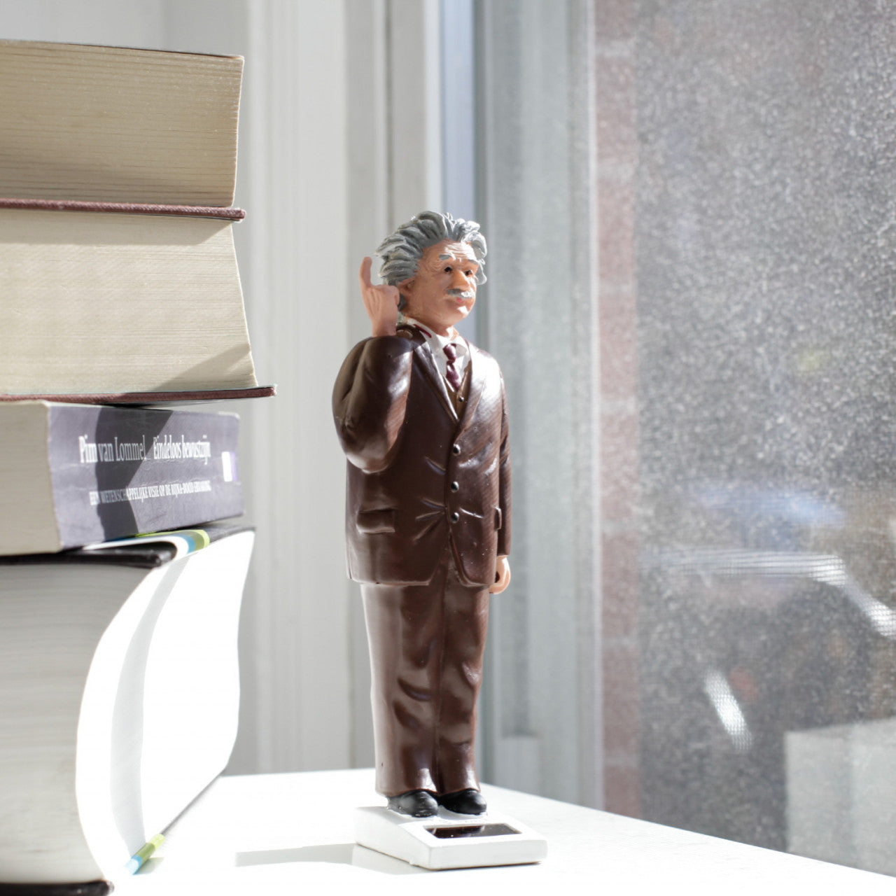Die Dekofigur Einstein mit Solarantrieb steht neben gestapelten Büchern auf einer sonnenbeschienenen Fensterbank.