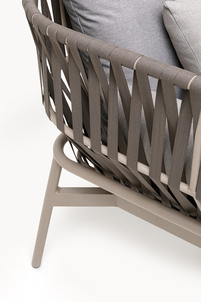 Nahaufnahme eines modernen Stuhls mit taupefarbenem Gestell, geflochtener Riemenrückenlehne und hellgrauen Polstern.