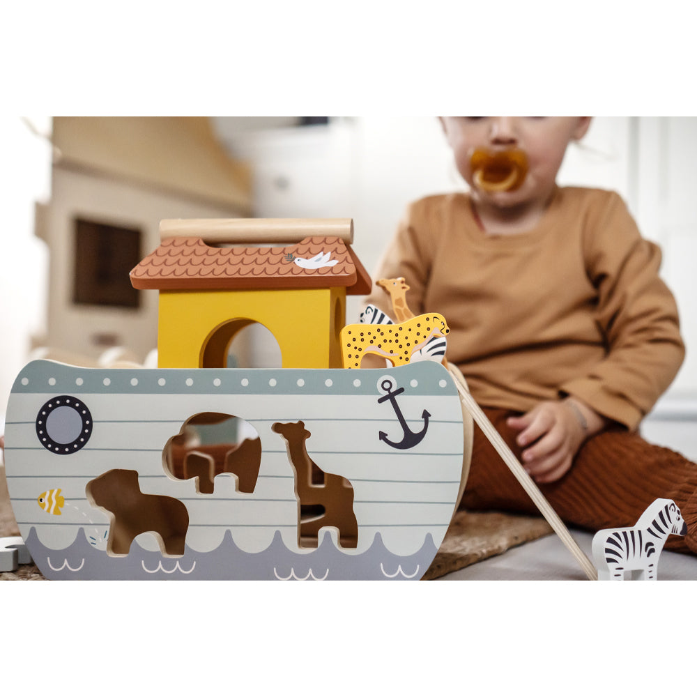 Ein Kleinkind spielt mit dem Steckspiel Arche Noah „Safari“, trägt braune Kleidung und hält einen Schnuller.