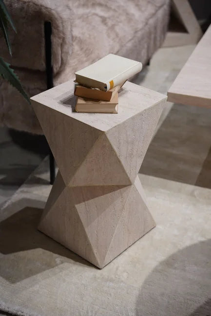Ein geometrischer Beistelltisch aus Holz, auf dem drei geschlossene Bücher gestapelt sind, neben einer Couch.