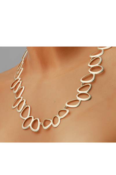 Eine Person trägt die auffällige goldene Halskette „Judith Martini: Schmuckset „Petit Bijou“ mit großen, unregelmäßig ovalen Gliedern auf nackter Haut.