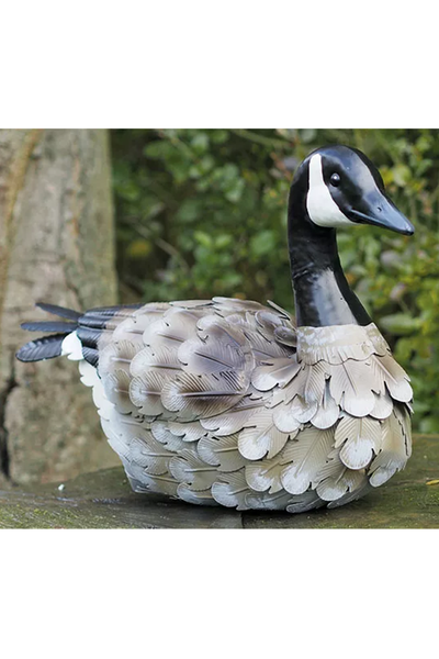 Die Gartenfigur „Kanadagans“ ist eine realistische Kanadagans-Attrappe aus Kunststoff, die im Freien neben einem Baum inmitten üppigen Grüns aufgestellt wird.
