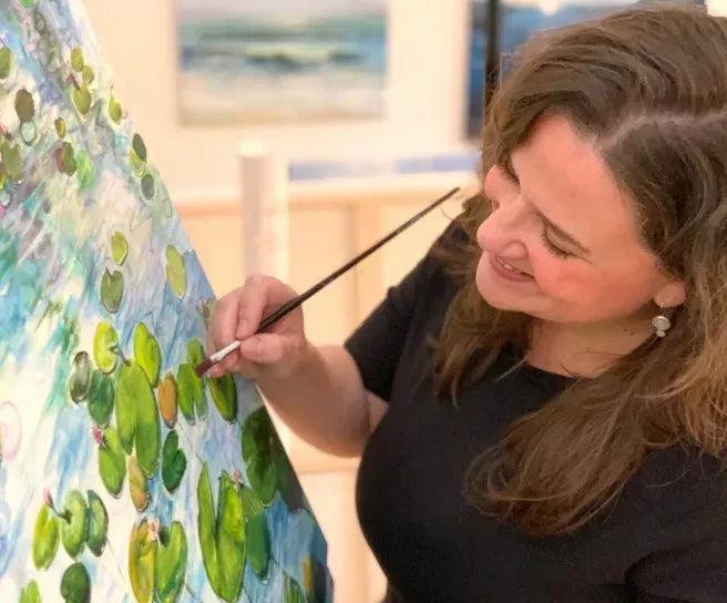 Eine Frau malt grüne Seerosenblätter auf eine bunte Leinwand und stellt in einem Kunstatelier Sandra Gebhardt-Höpfners gerahmtes Kunstwerk „Summer Garden 2“ (2023) nach.