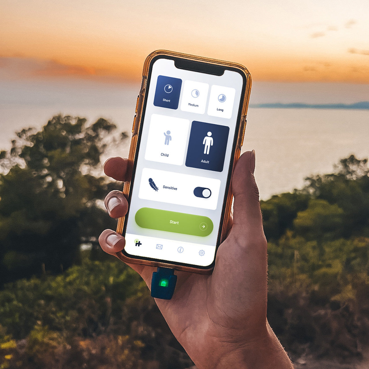Eine Hand hält ein Smartphone mit geöffneter Lightning-App „Insektenstichheiler heat it“ vor dem Hintergrund eines malerischen Sonnenuntergangs über Wasser und Bäumen.