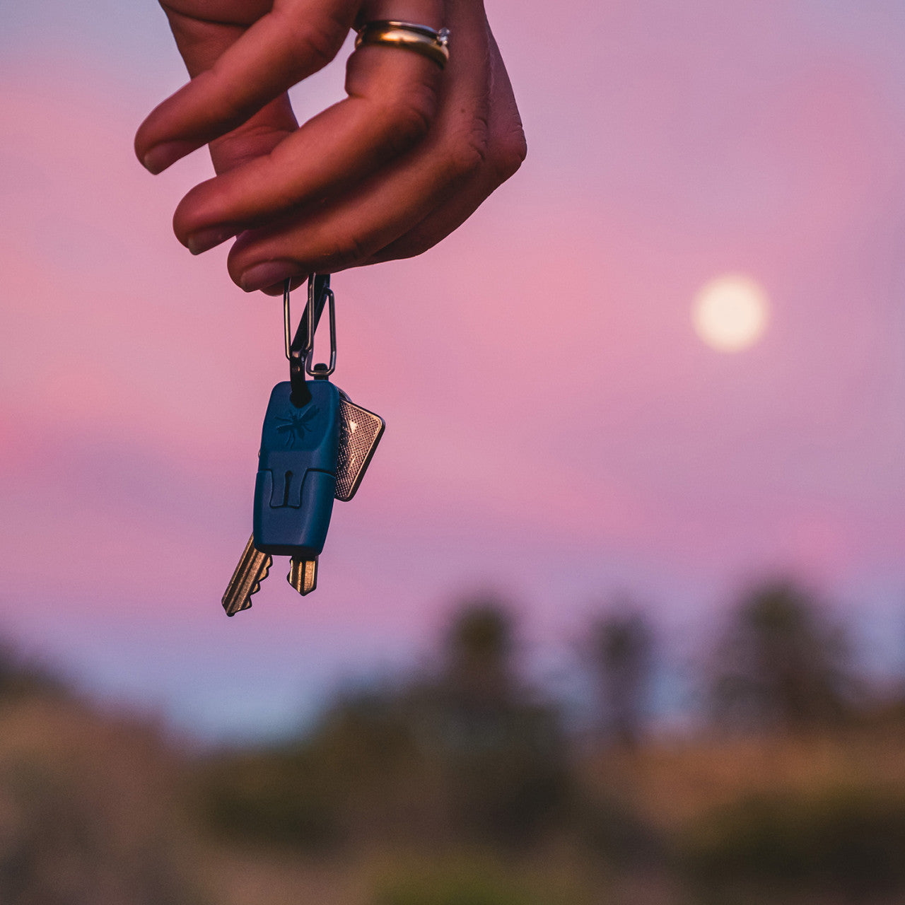Eine Hand hält den Insektenstichheiler Heat It Classic Lightning vor einem Sonnenuntergangshimmel mit Vollmond und unscharfer Landschaft im Hintergrund.
