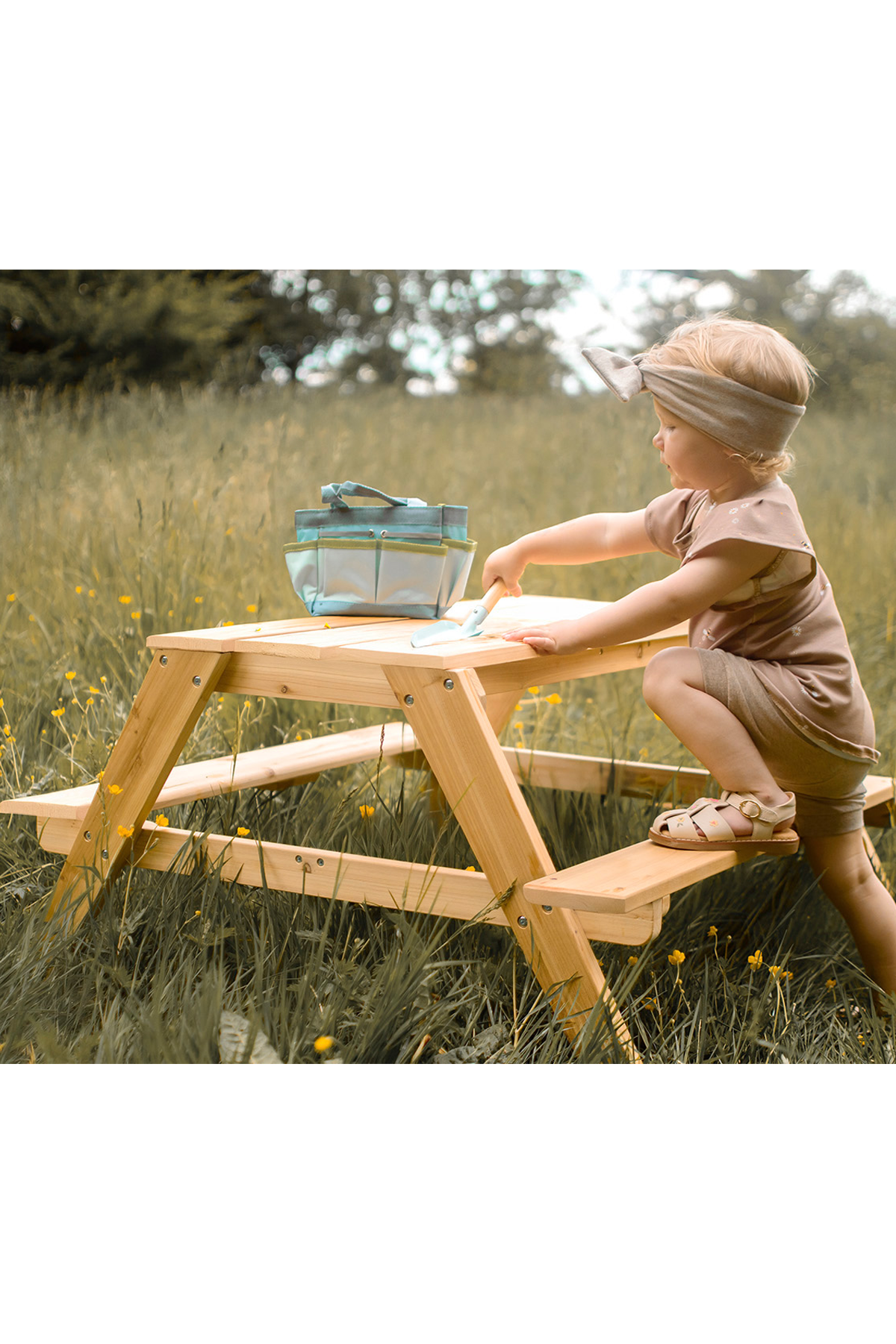 Picknicktisch aus Holz mit beidseitig angebrachten Bänken, für den Außenbereich mit einem Mädchen am Tisch in der Natur. 