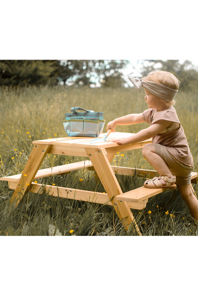 Picknicktisch aus Holz mit beidseitig angebrachten Bänken, für den Außenbereich mit einem Mädchen am Tisch in der Natur. 