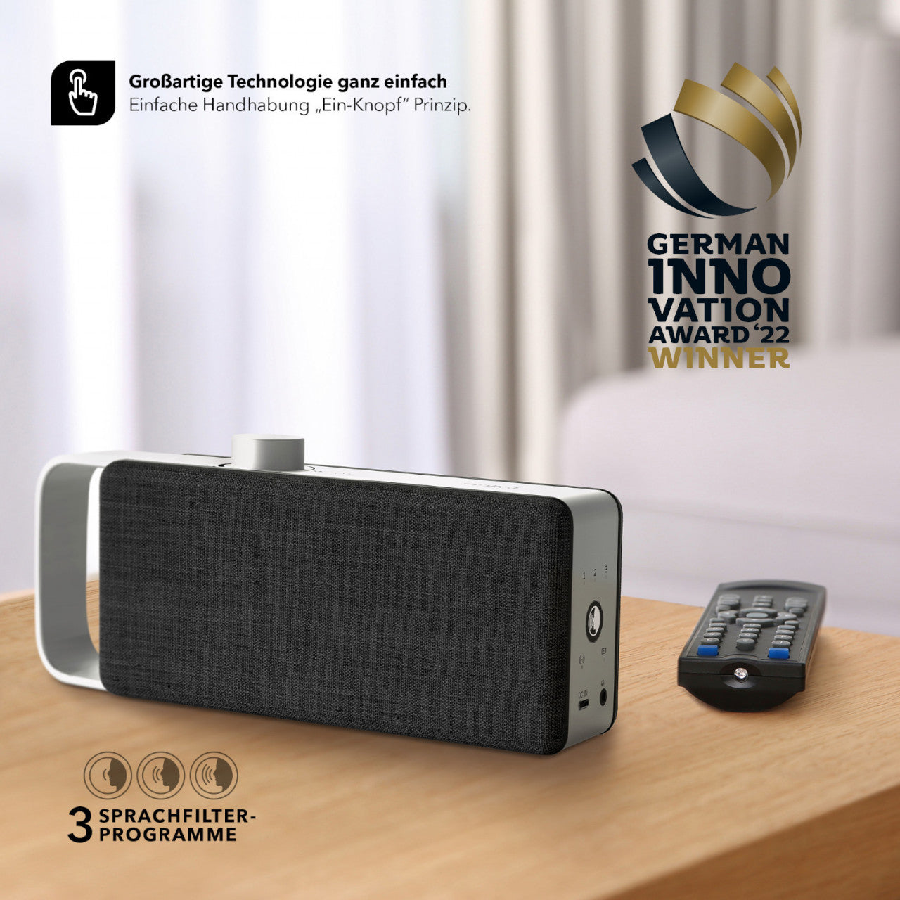 Ein moderner schwarz-weißer OSKAR Tragbarer TV-Sprachverstärker und eine Fernbedienung auf einem Tisch mit dem Logo des German Innovation Award 22 Winner.