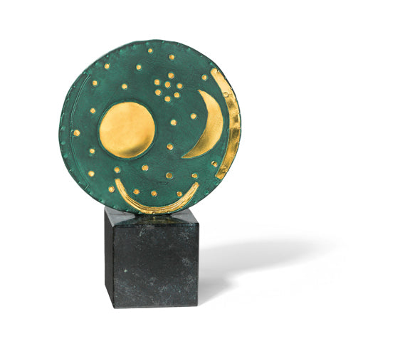Runde Skulptur in Grün und Gold mit Himmelssymbolen auf einem dunklen quadratischen Sockel vor einem weißen Hintergrund.