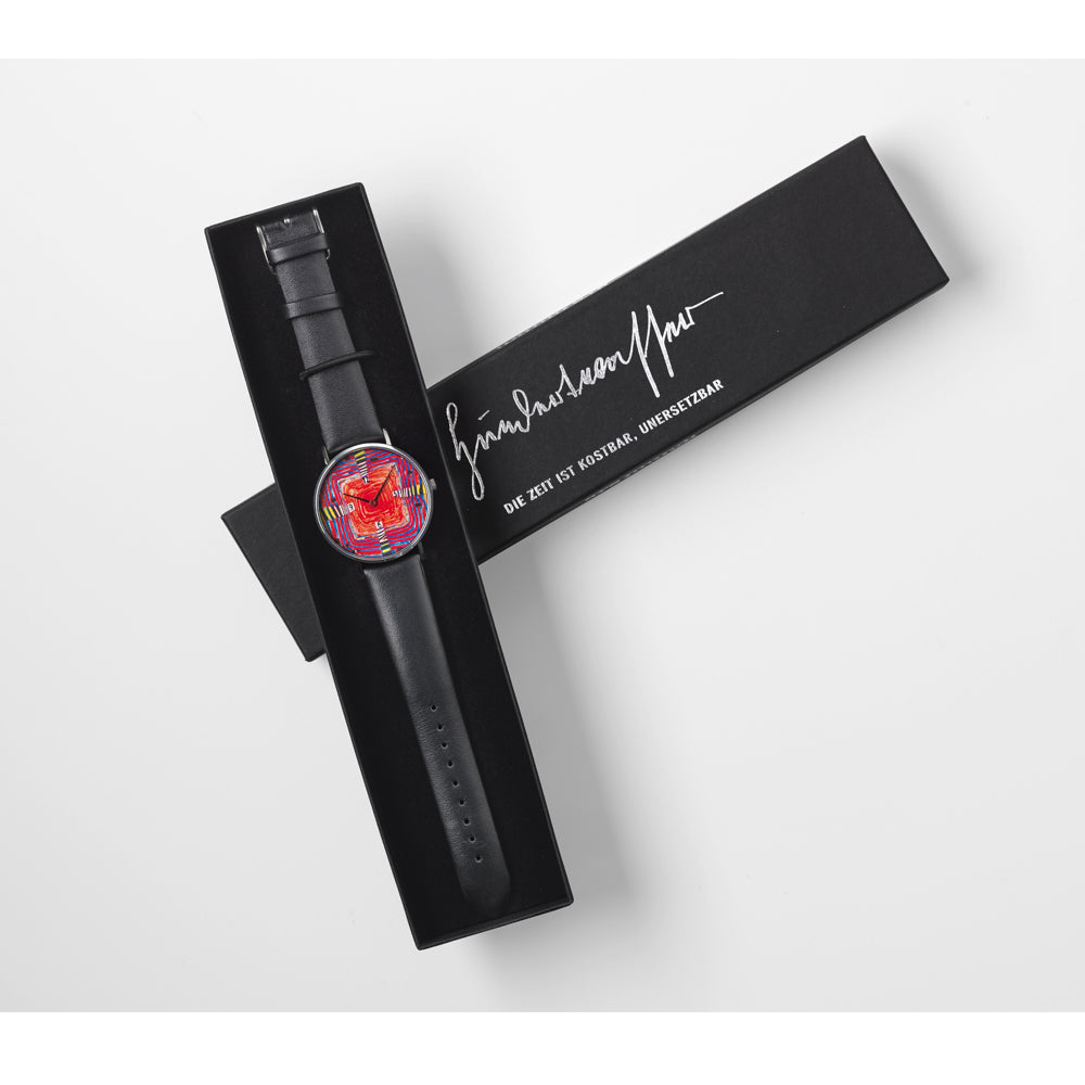 Eine schwarze Armbanduhr mit einem farbenfrohen abstrakten Zifferblatt, präsentiert auf einer schwarzen Box mit weißem Signaturtext.