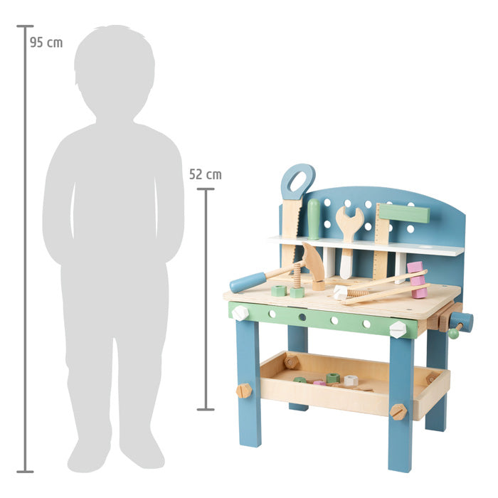 Die Holzspielzeugwerkbank Werkbank kompakt „Nordic“, abgebildet mit Werkzeug und Zubehör neben einer Messlatte mit der Silhouette eines Kindes als Maßstab.