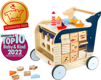 Der Lauflernwagen Wal ist ein hölzerner Aktivitäts-Lauflernwagen mit Blöcken und Formen zum Thema Ozean, auf dessen linker Seite Auszeichnungsabzeichen angezeigt werden.