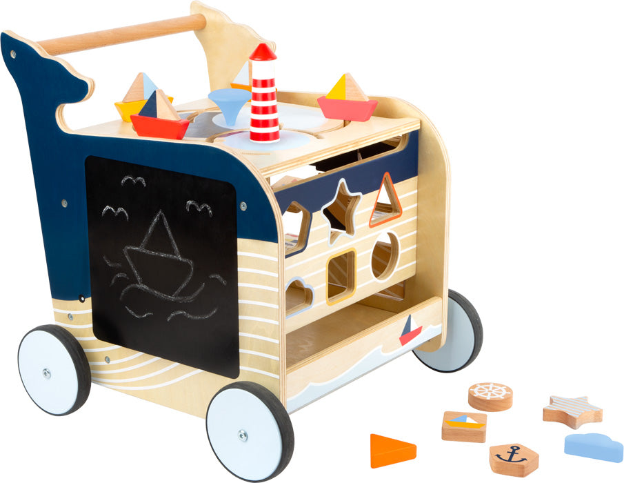 Der Lauflernwagen Wal ist ein hölzerner Lauflernwagen mit nautischem Thema, der über einen Formensortierer, eine Tafel und bunte Bodenformen verfügt.