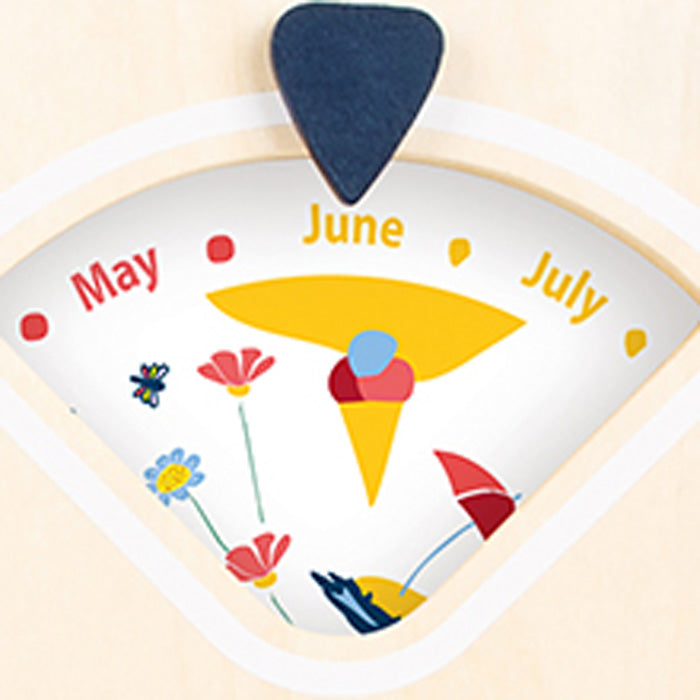 Die Lernuhr mit Kalender „Educate“ verfügt über ein Kalenderzifferblatt, das auf Juni zeigt, mit Blumen- und Sommerillustrationen unter den Monaten Mai, Juni und Juli.