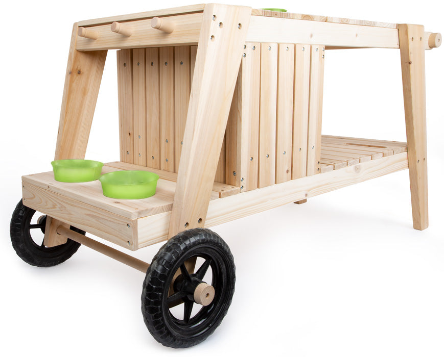 Die Matschküche ist ein fahrbarer Holzwagen mit zwei schwarzen Rädern und grünen Schüsseln auf der unteren Ablage.