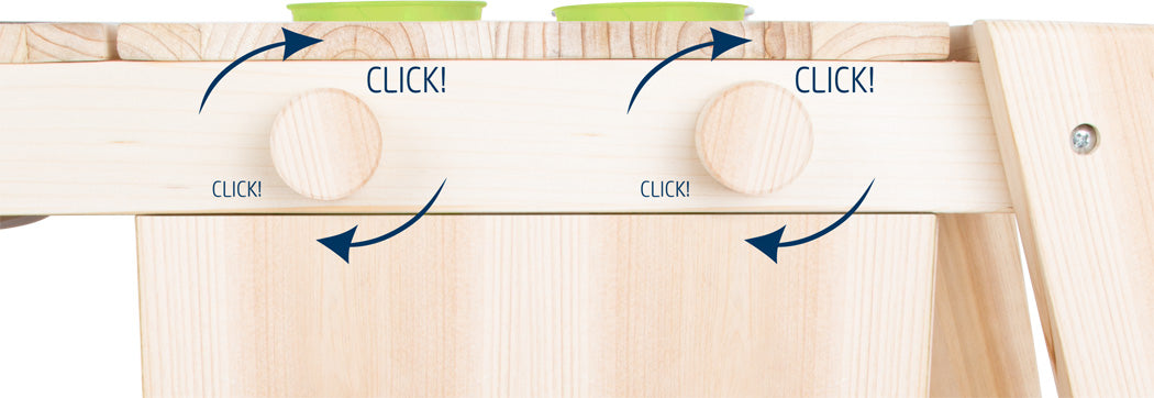 Nahaufnahme der Matschküche-Holzknöpfe mit Pfeilen und dem Wort „KLICK!“, das auf einen Dreh- oder Verriegelungsmechanismus hinweist.