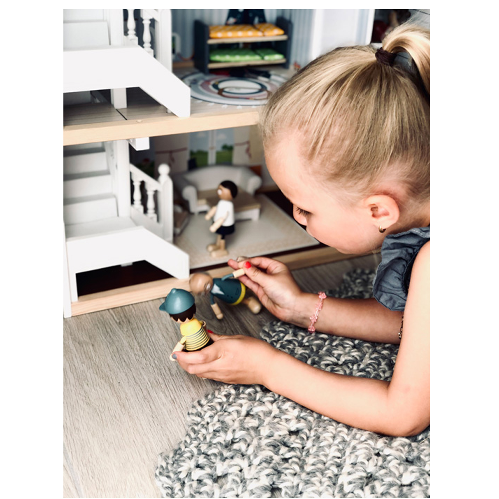 Ein junges Mädchen spielt in ihrer Puppenhaus-Stadtvilla mit Holzpuppen auf einem weichen, strukturierten Teppich.