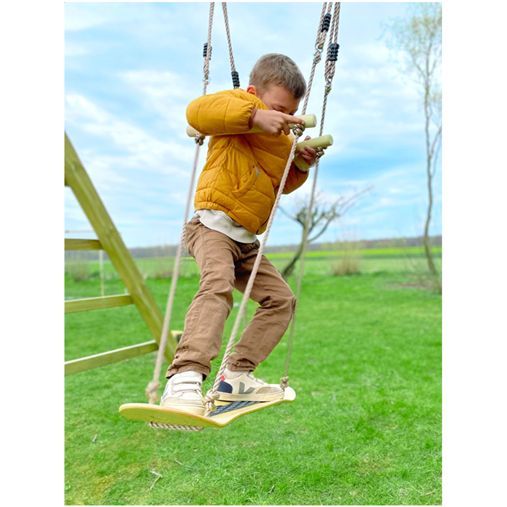 Ein kleiner Junge in einer gelben Jacke genießt die Natur auf einer Wiese, sitzt auf einer Skateboard-Schaukel und schaut auf ein Handgerät.