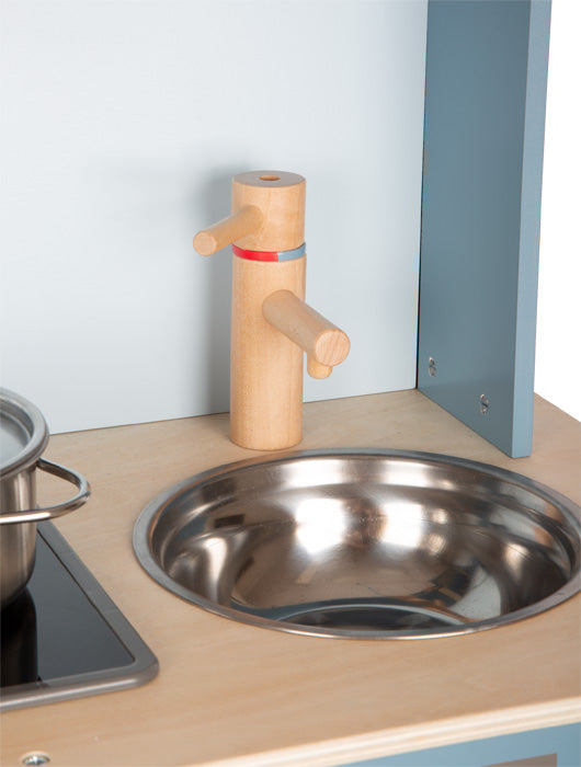 Das Kinderküche-Spielküchenset „lecker“ verfügt über eine Metallspüle, einen Wasserhahn aus Holz und einen Topf auf dem Herd neben der Spüle.