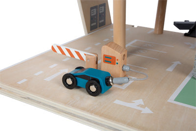 Ein Parkhaus Rallye-Spielzeugauto nähert sich einem gestreiften Schrankentor im hölzernen Parkplatz-Spielset.