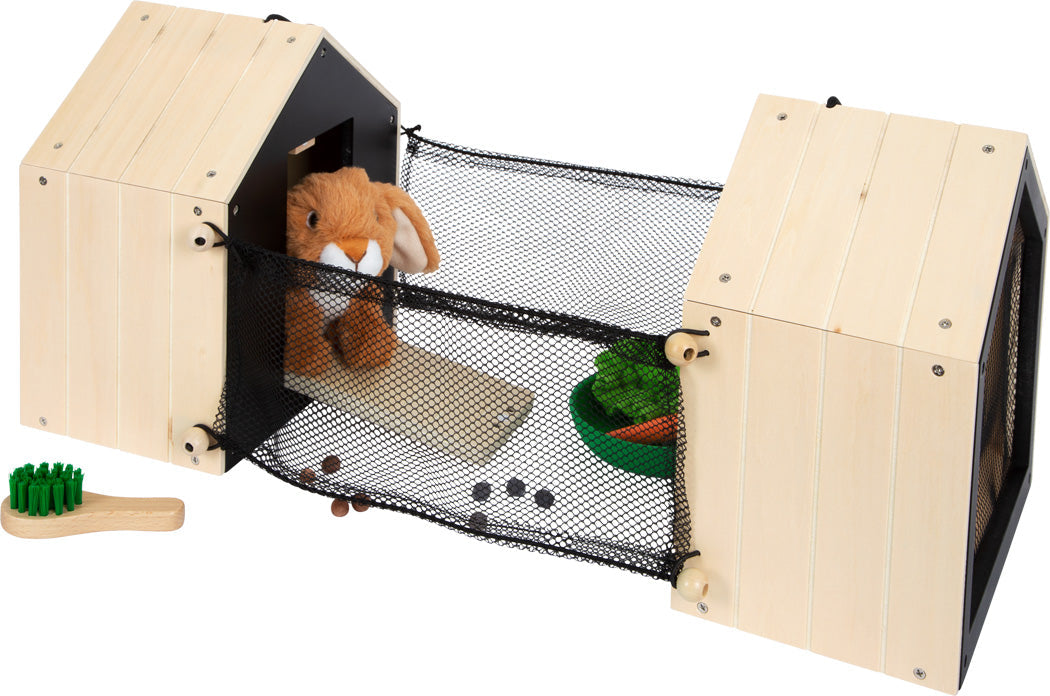 Der Hasenstall mit Auslauf umfasst ein Spielzeughäschen in einem Holzspielhaus mit einem Netztunnel, Spielzeugfutter und einer kleinen grünen Bürste in der Nähe.