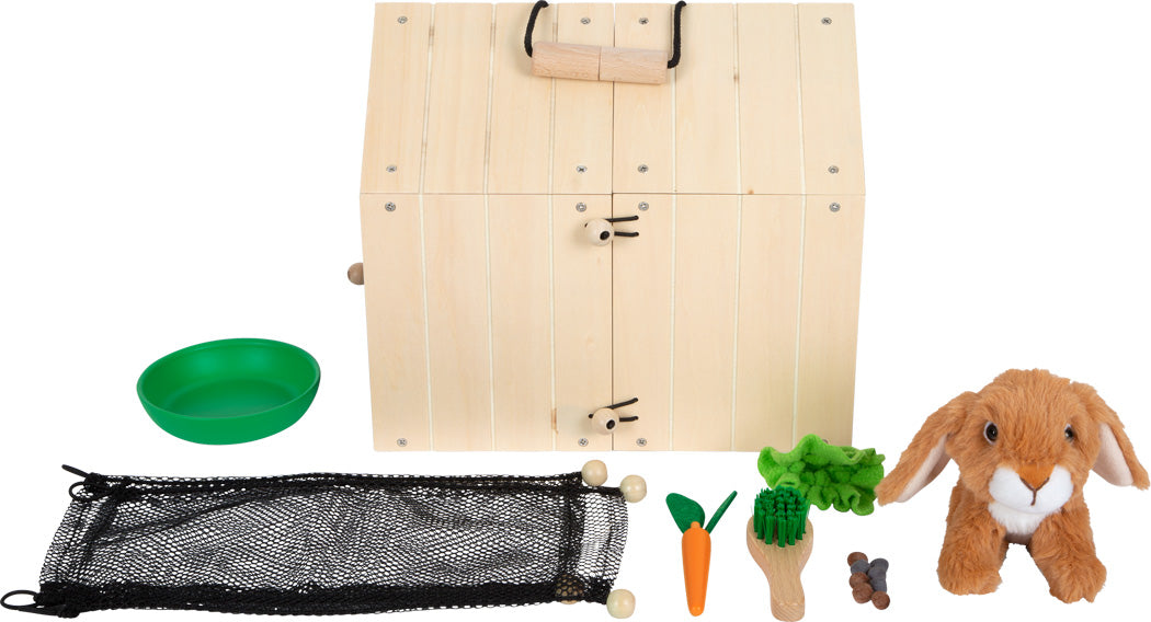 Das Set „Hasenstall mit Auslauf“ enthält eine hölzerne Transportbox, ein Plüschkaninchen, eine grüne Schüssel, eine Spielzeugkarotte, Salat, eine Schaufel und ein schwarzes Netz.
