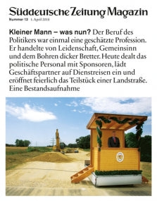 An einer Landstraße steht ein kleines Wachhaus mit einem Mann im Anzug und einer Statue im Hintergrund.