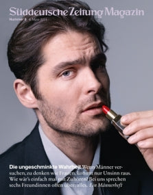 Ein Mann im Anzug hält einen roten Lippenstift an seine Lippen und schaut nachdenklich in die Kamera.