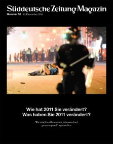 Ein Polizeibeamter steht im Mittelpunkt, während im Hintergrund Menschen während einer nächtlichen Demonstration auf der Straße sitzen.