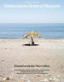 Eine Person sitzt allein unter einem Strohschirm an einem einsamen Strand am ruhigen Meer.