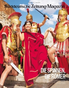 Eine lächelnde Frau in einer roten Toga posiert mit Menschen, die als römische Soldaten in antiker Kleidung gekleidet sind.