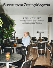 Ein Mann sitzt allein an einem Tisch in einem leeren Café mit schwarzen Stühlen und kleinen runden Tischen.