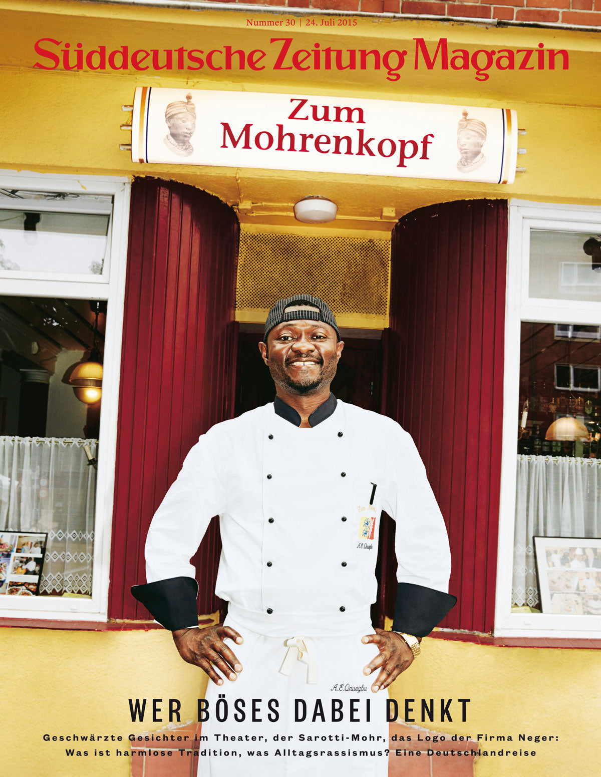 Ein lächelnder Koch in Weiß steht vor dem Restaurant Zum Mohrenkopf, unter einem Schild mit einer Karikatur.