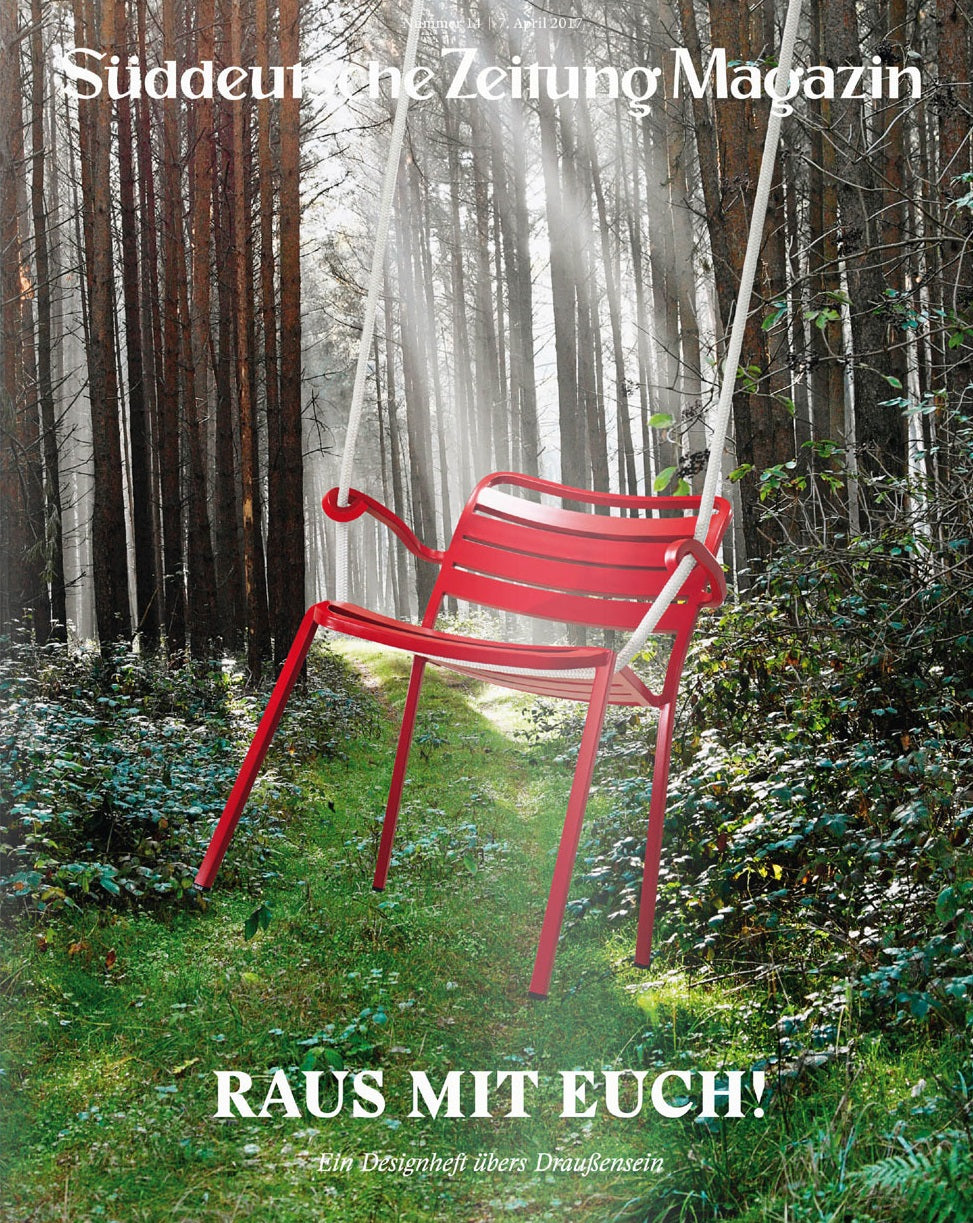 Ein roter Stuhl hängt als Schaukel in einem sonnenbeschienenen Waldweg; unten steht der Text RAUS MIT EUCH!.