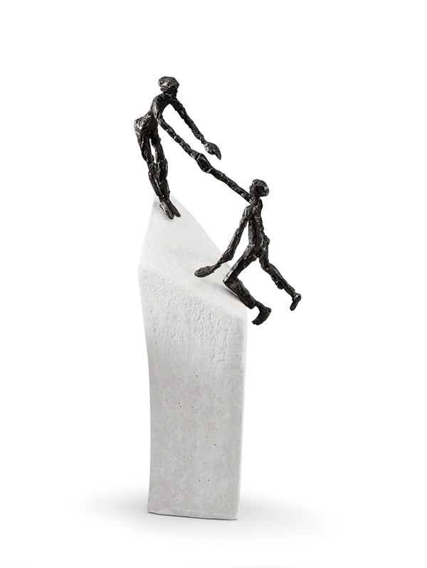 Eine Metallskulptur einer Figur, die einer anderen beim Erklimmen eines hohen, weißen, abstrakten Sockels hilft.