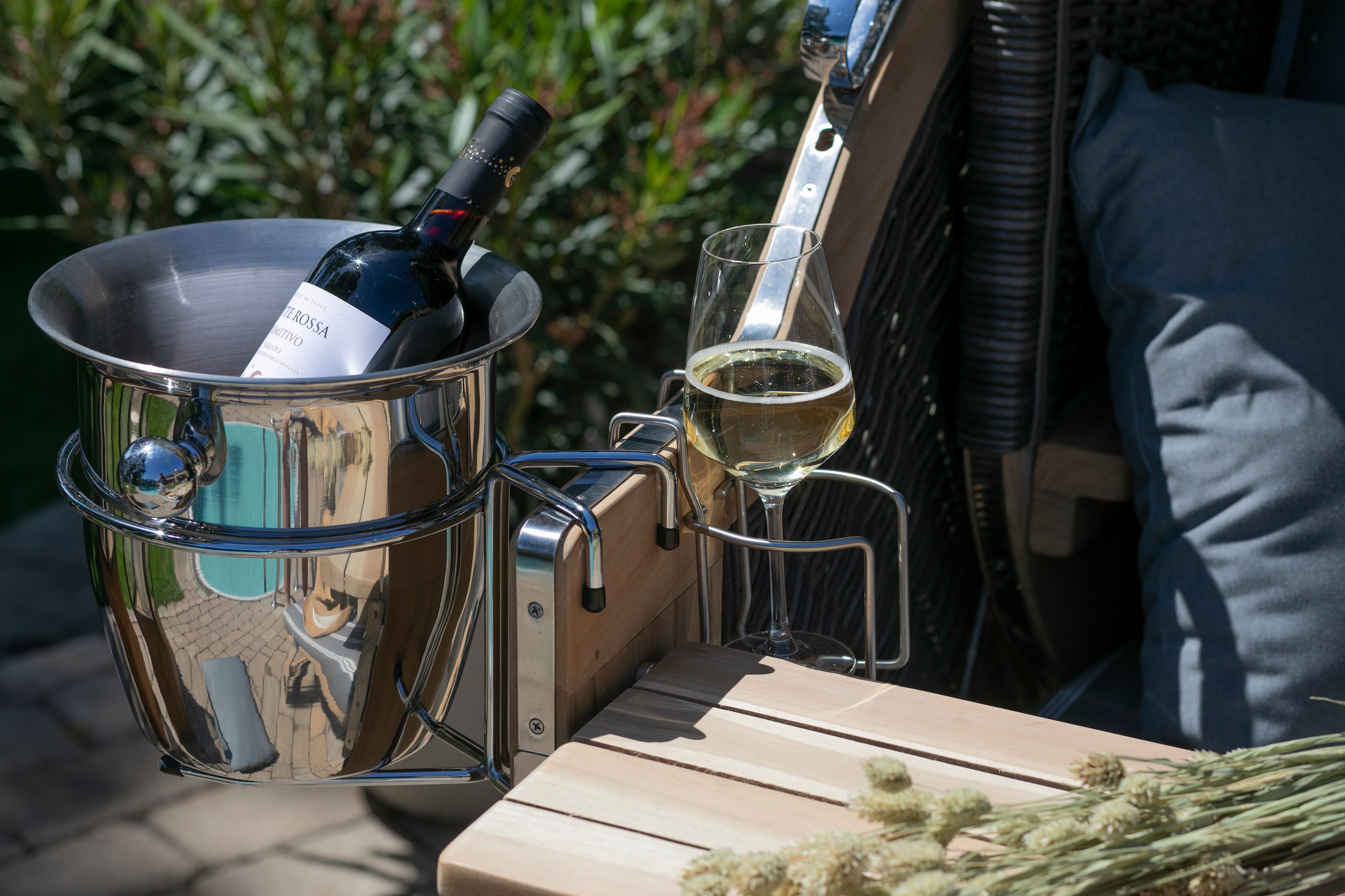 Eine Weinflasche in einem Eiskübel und ein Glas Weißwein auf einer Holzbank im Freien.
