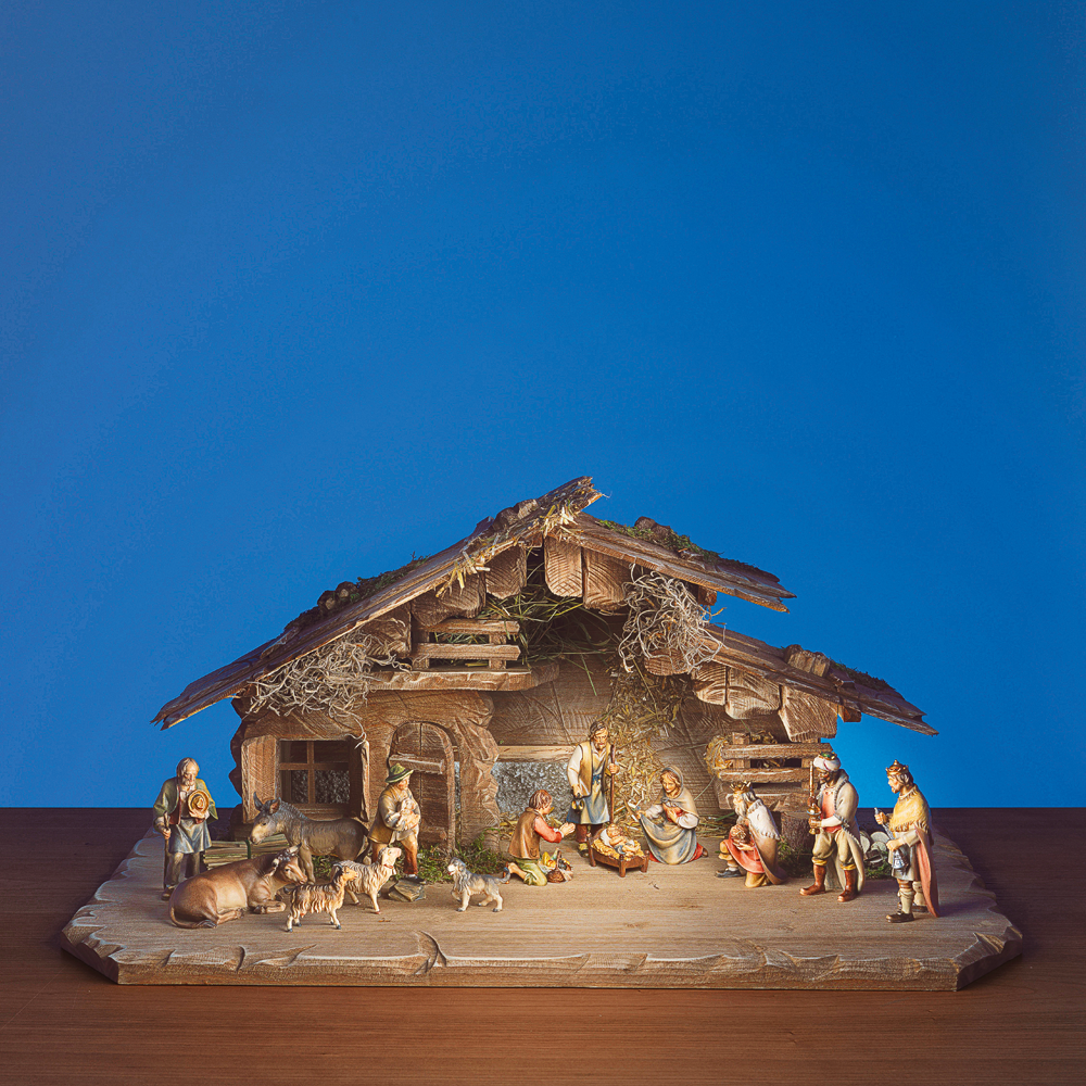 Eine Weihnachtskrippe mit Figuren von Menschen und Tieren in einem Holzstall vor blauem Hintergrund.