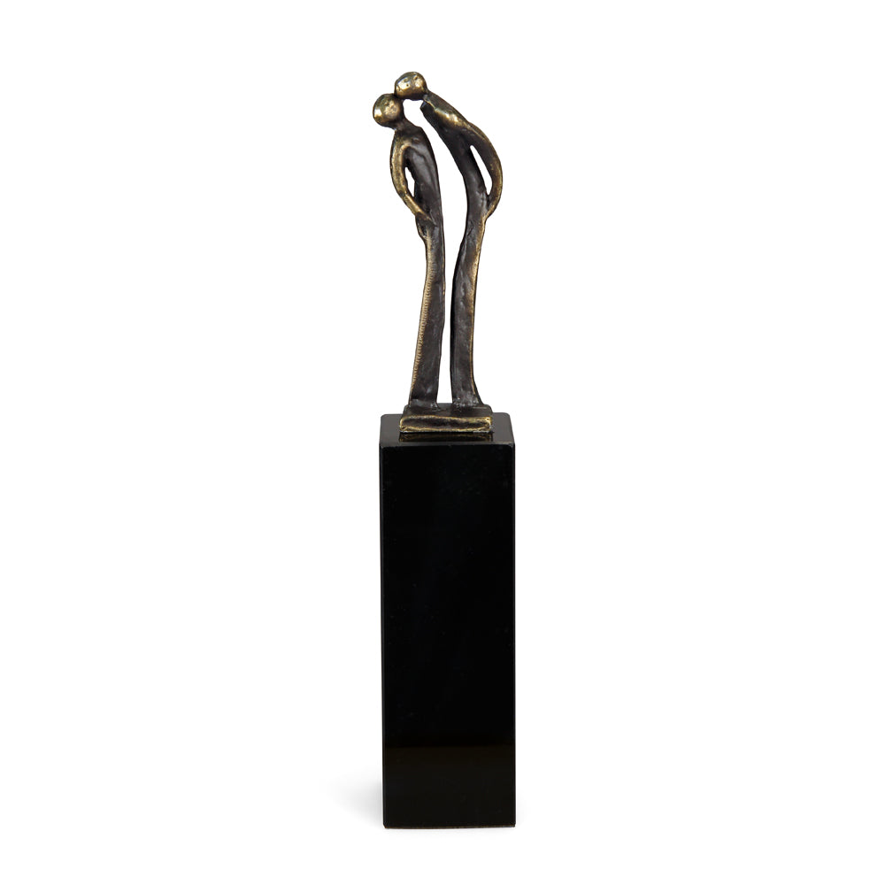 Abstrakte Bronzeskulptur zweier sich umarmender Figuren auf einem hohen, schwarzen rechteckigen Sockel.