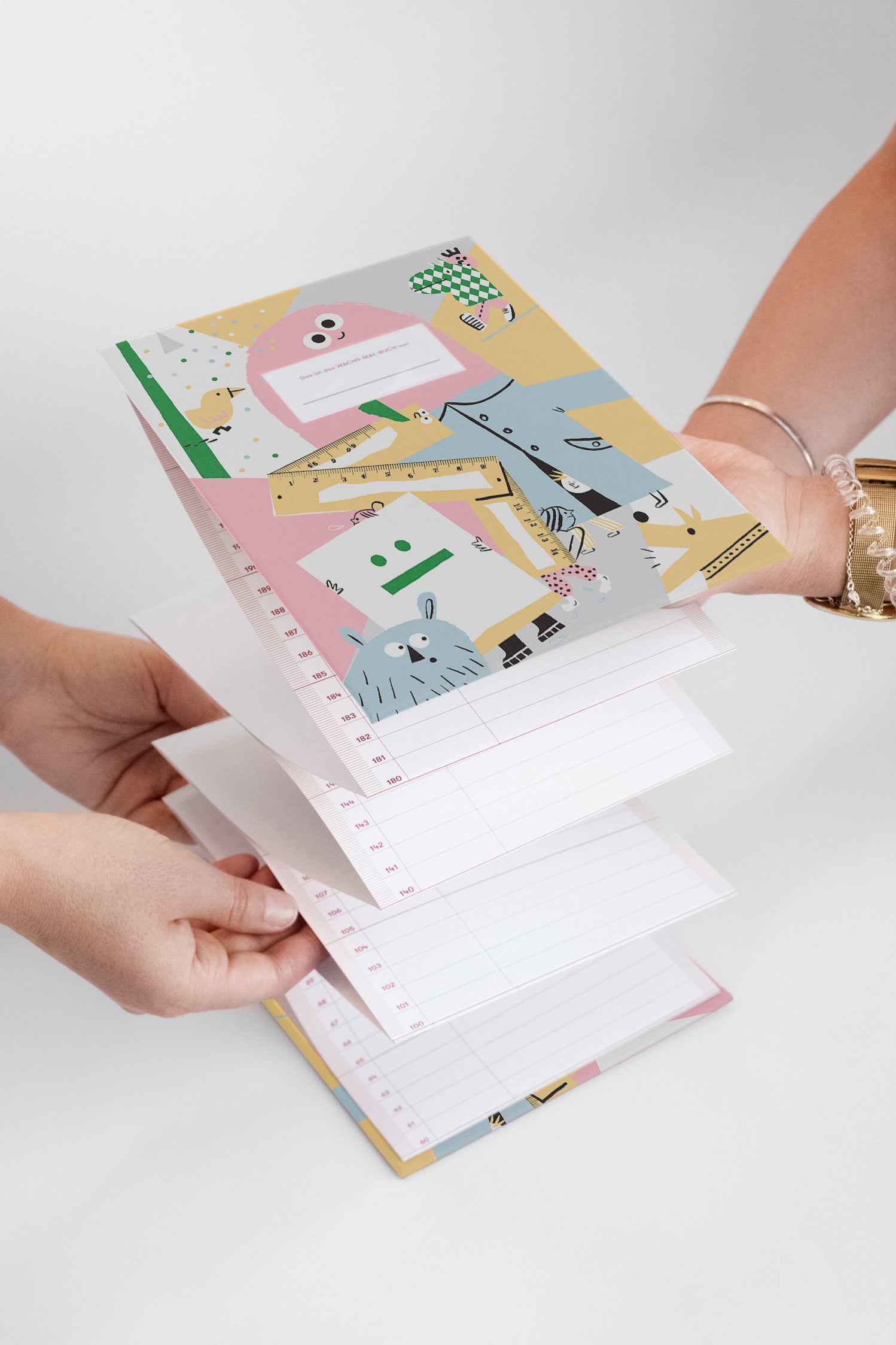Zwei Personen halten ein buntes, illustriertes Notizbuch mit aufklappbaren linierten Seiten in der Hand.